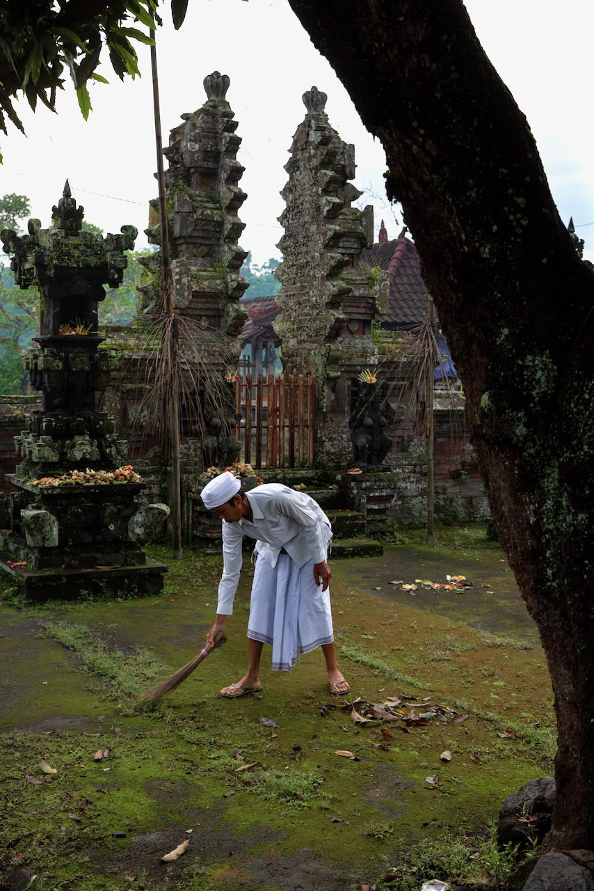 A man in white sweeps the ground before a temple gate.