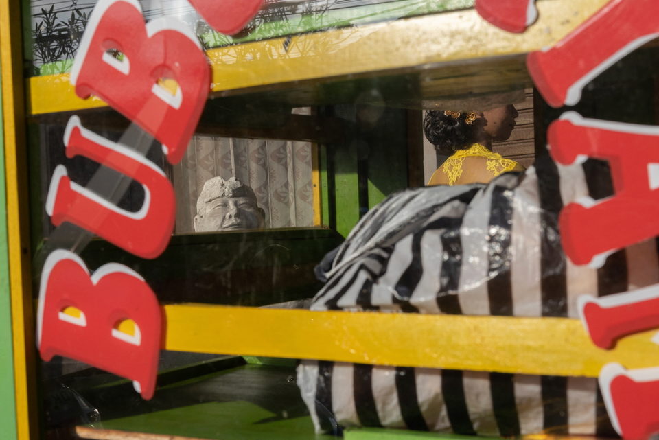 Red and yellow cart lettering over a figure in striped cloth beyond the glass.