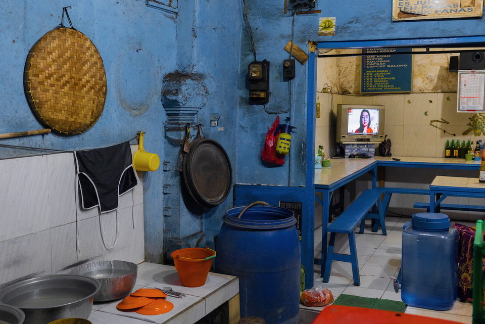 A blue-walled warung kitchen with a television on a high shelf.