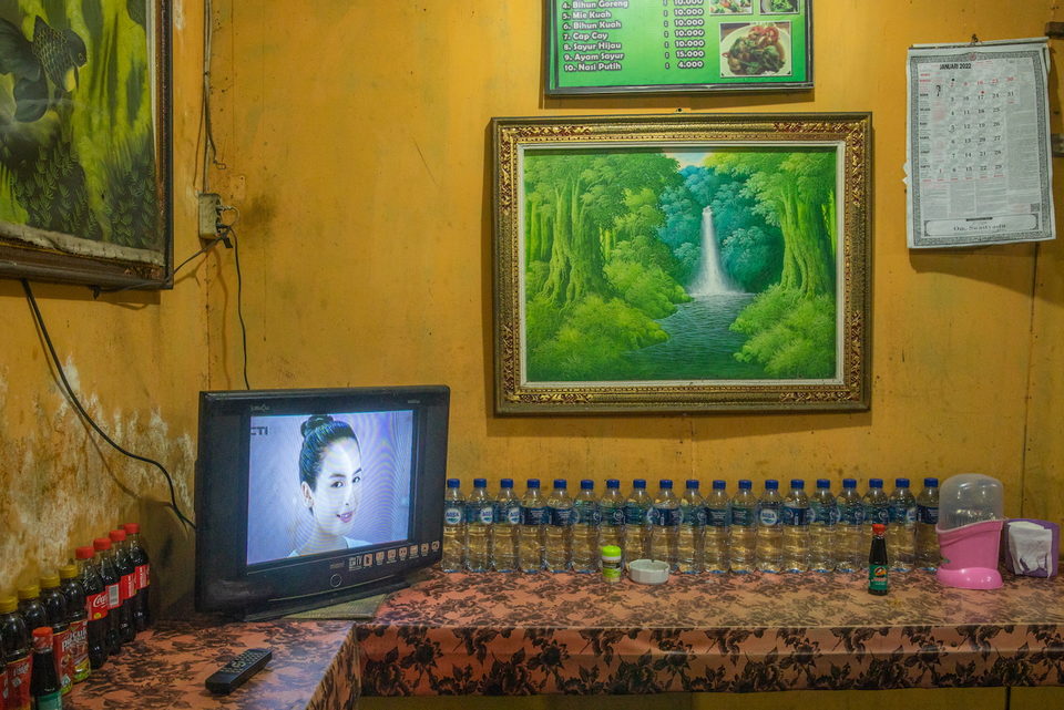A television below a framed painting of a waterfall, bottles along the counter.