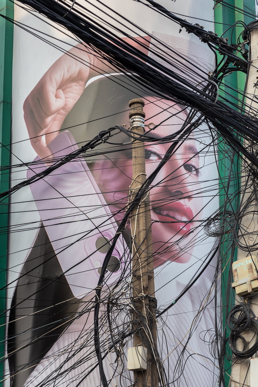 A billboard of a face behind a tangle of overhead cables.