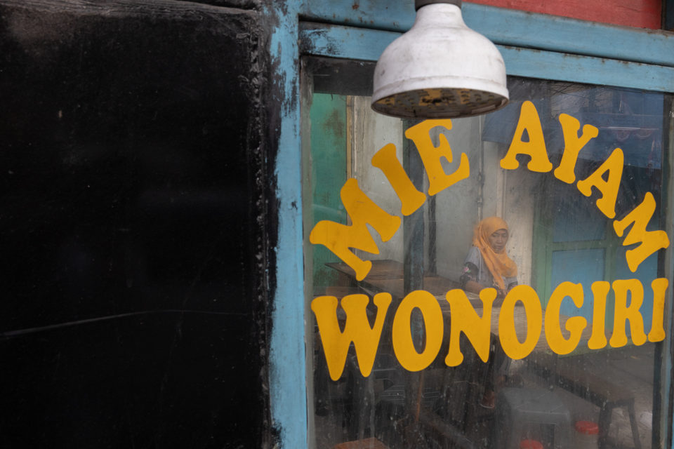 MIE AYAM WONOGIRI in yellow across the glass, a woman in a yellow headscarf inside.