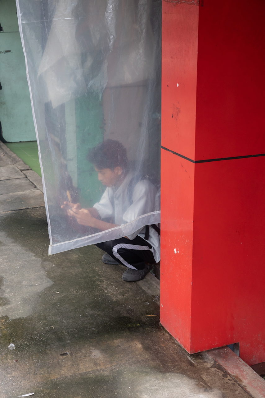 A man crouches behind a clear plastic sheet, lit by his phone.