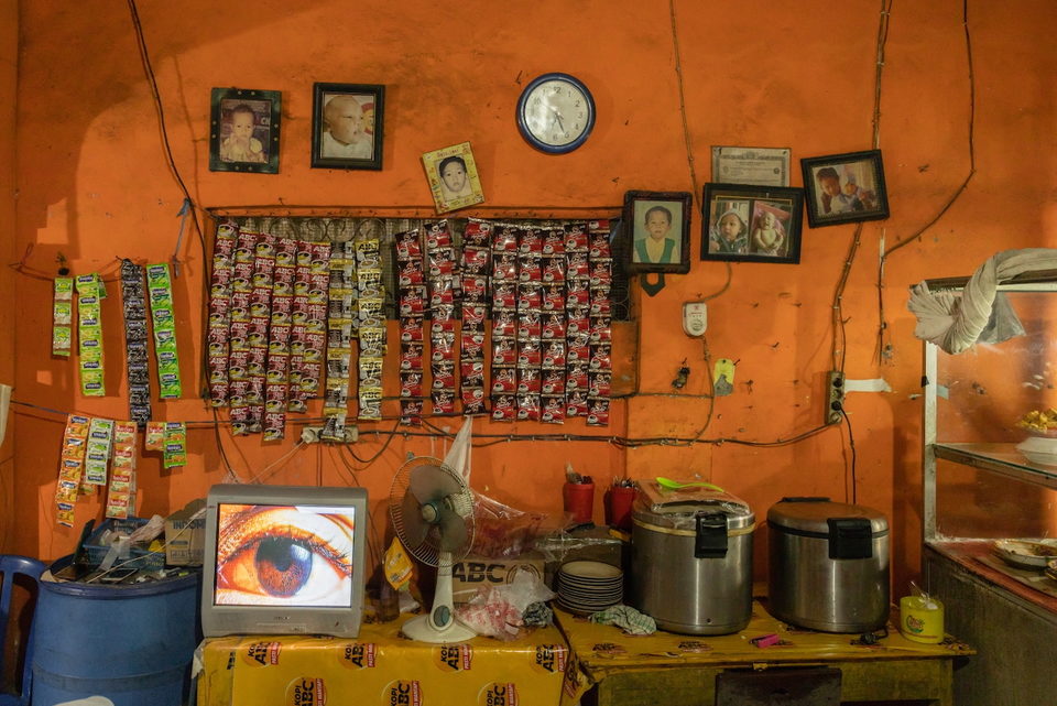 An orange warung wall hung with framed photographs and sachet packets.
