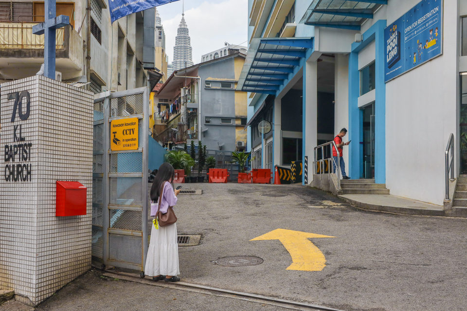 A street in Kuala Lumpur with the Petronas Towers beyond, a woman in white walking.