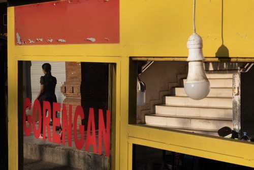 A yellow food cart window with red lettering, a staircase and bare bulb beyond.