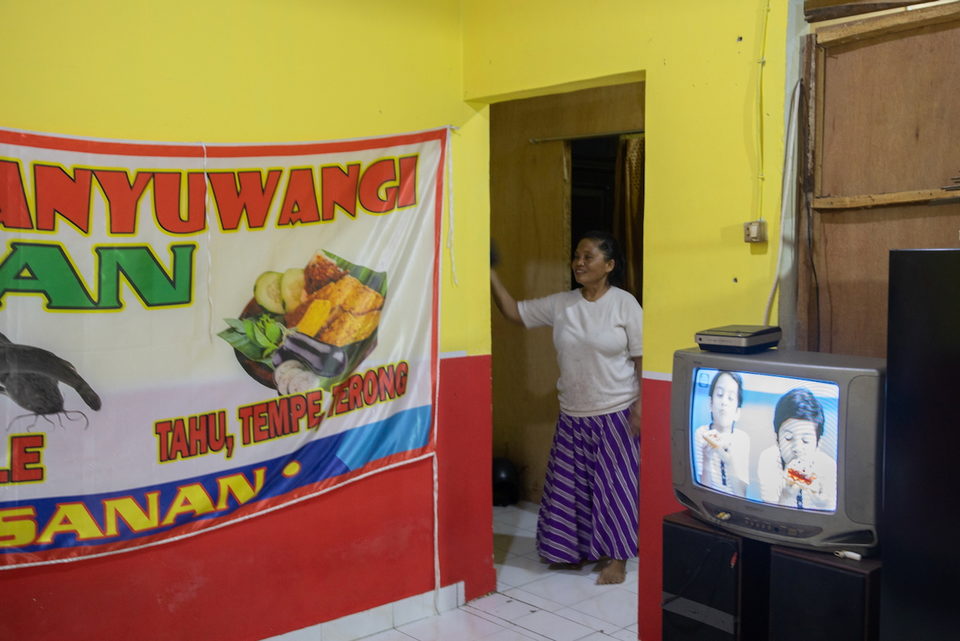 A woman stands in a doorway beside a food banner and a television.