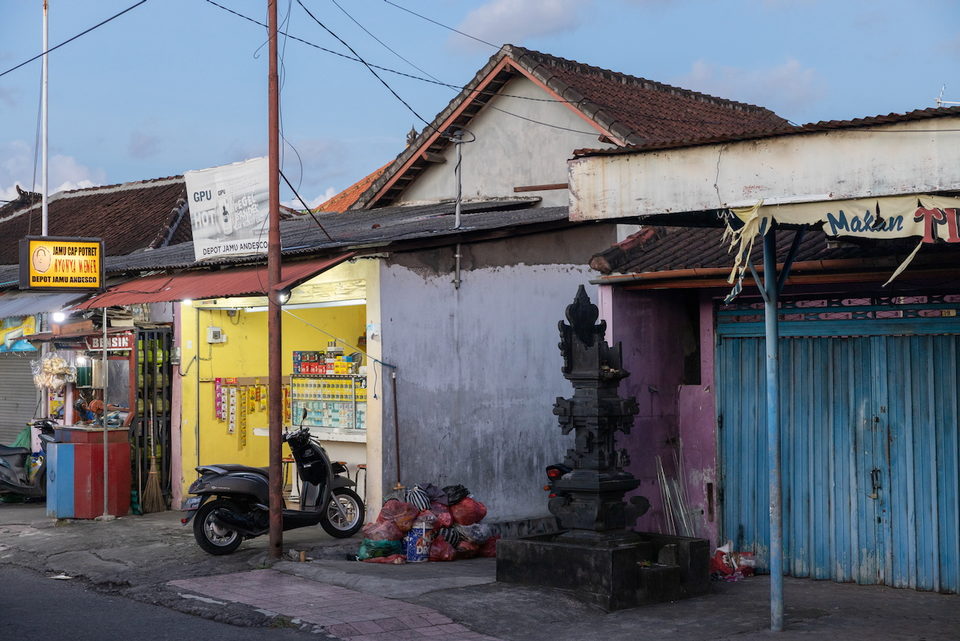 A quiet Balinese street of pink and yellow houses with a family shrine and a parked motorbike.
