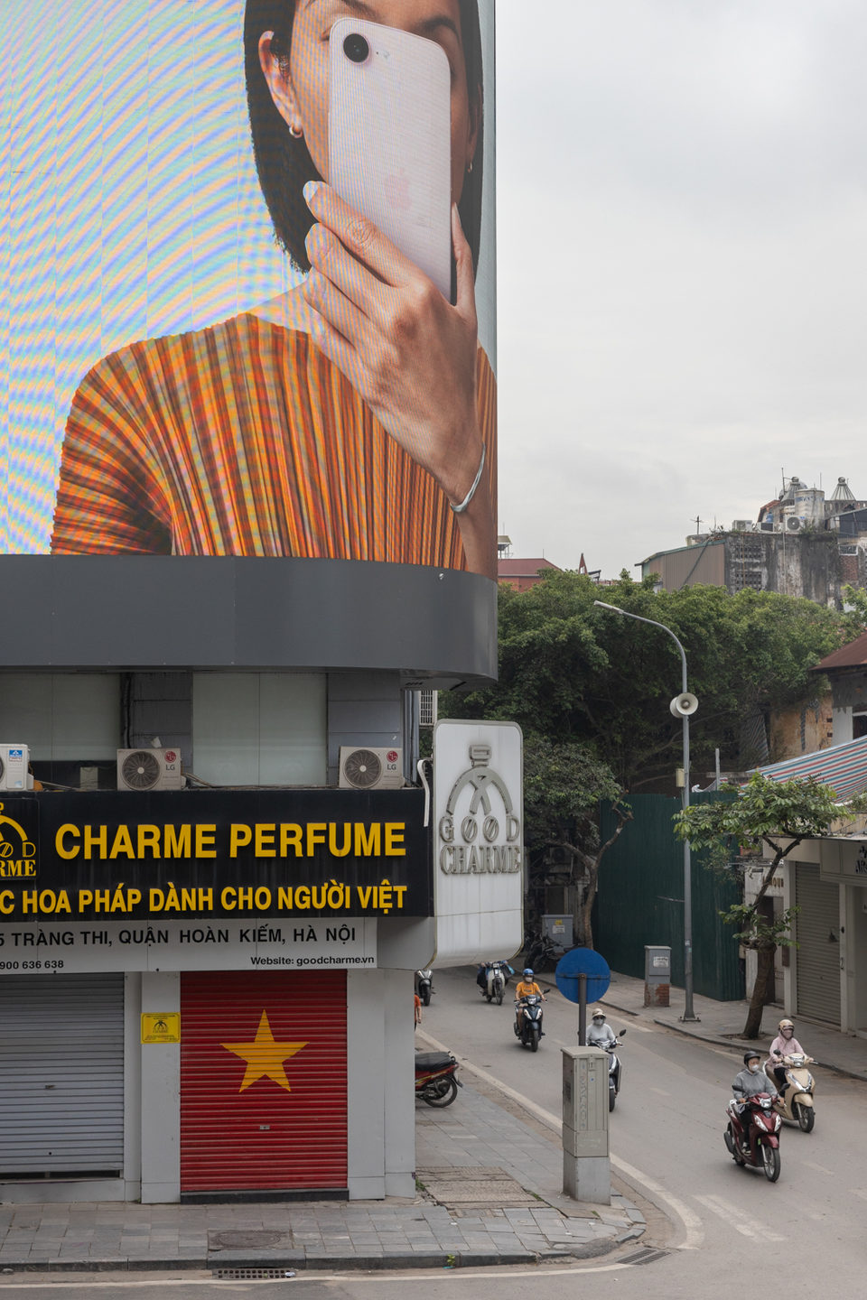 A billboard of a hand and an orange fan above a perfume shop on a Hanoi street.