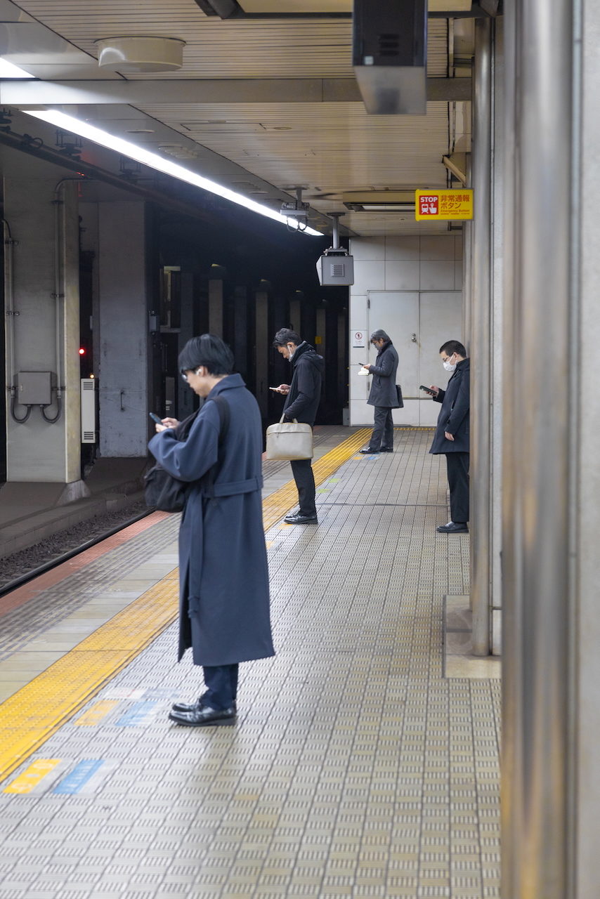 Commuters wait on a railway platform, one looking at his phone.