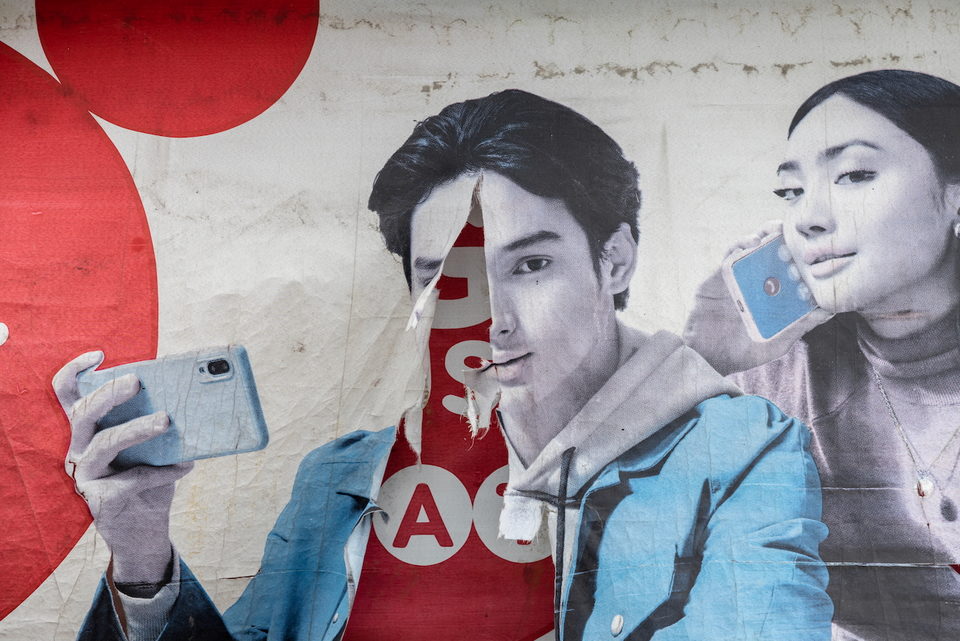 A weathered mural of a young man holding a phone, paint peeling from the wall.