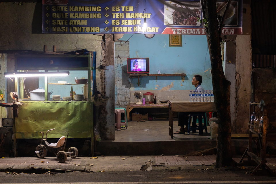 A roadside warung at night, a television glowing behind the counter.