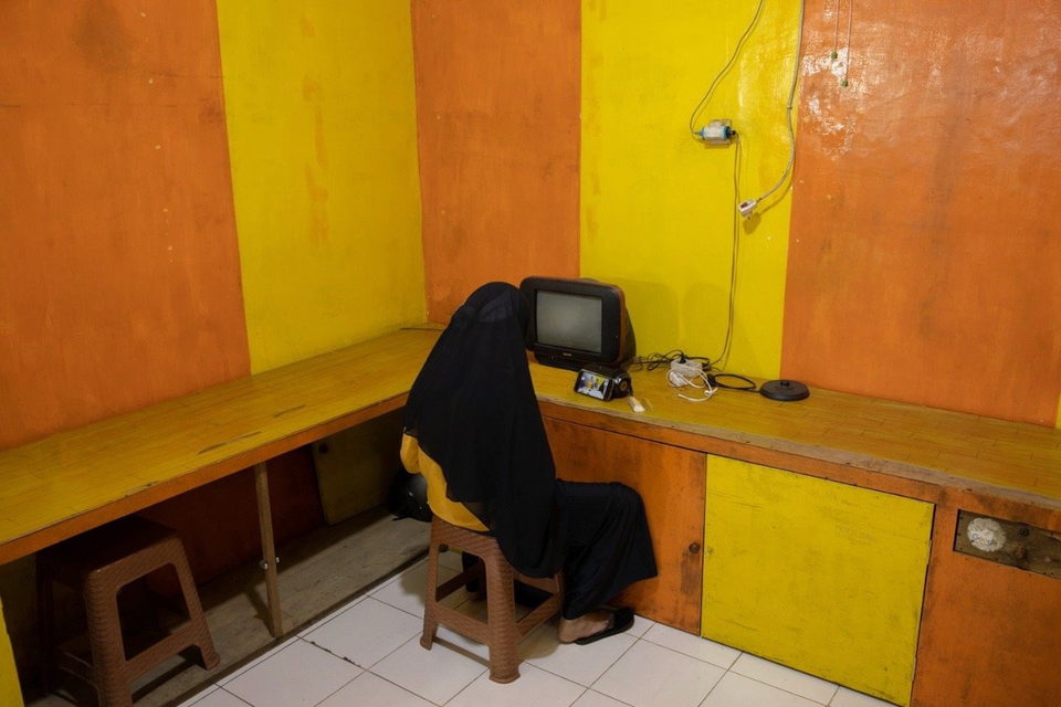 A person sits alone at a bench watching a small television against yellow and orange walls.