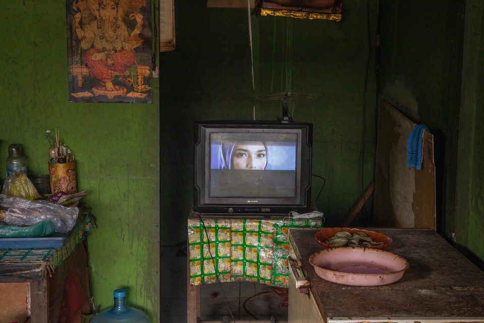 A television glowing in a dark warung above stacked sachets.