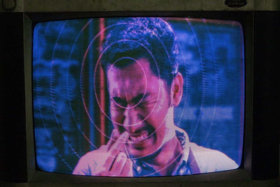 A television close-up of a man's face in blue and magenta.