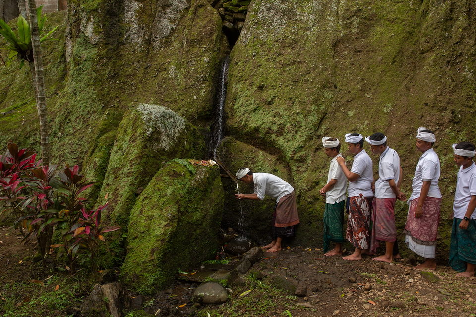 Worshippers gather at a spring beneath a mossy rock face.
