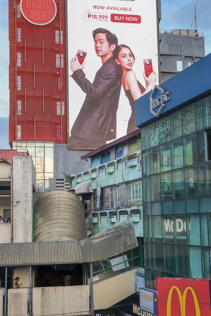 A billboard of a woman holding a phone above a glass-fronted building.