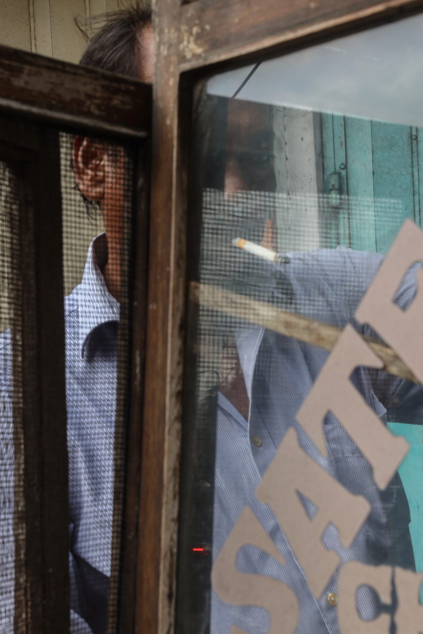 A man in a blue shirt behind a screen door, white letters across the glass.