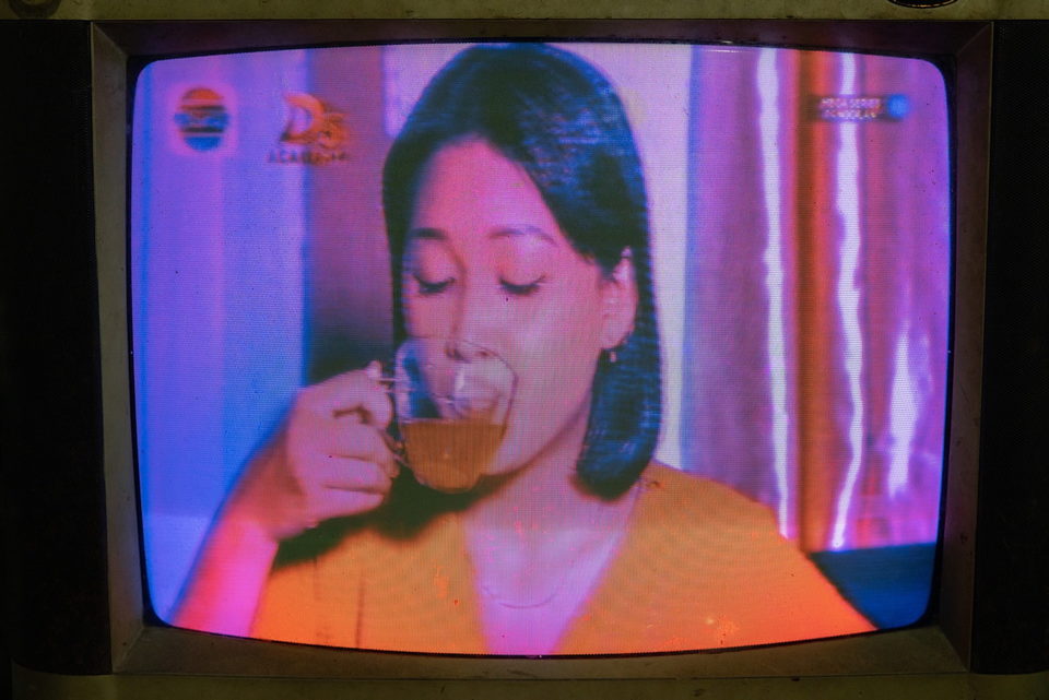 A television close-up of a woman drinking from a glass, the screen glowing pink.