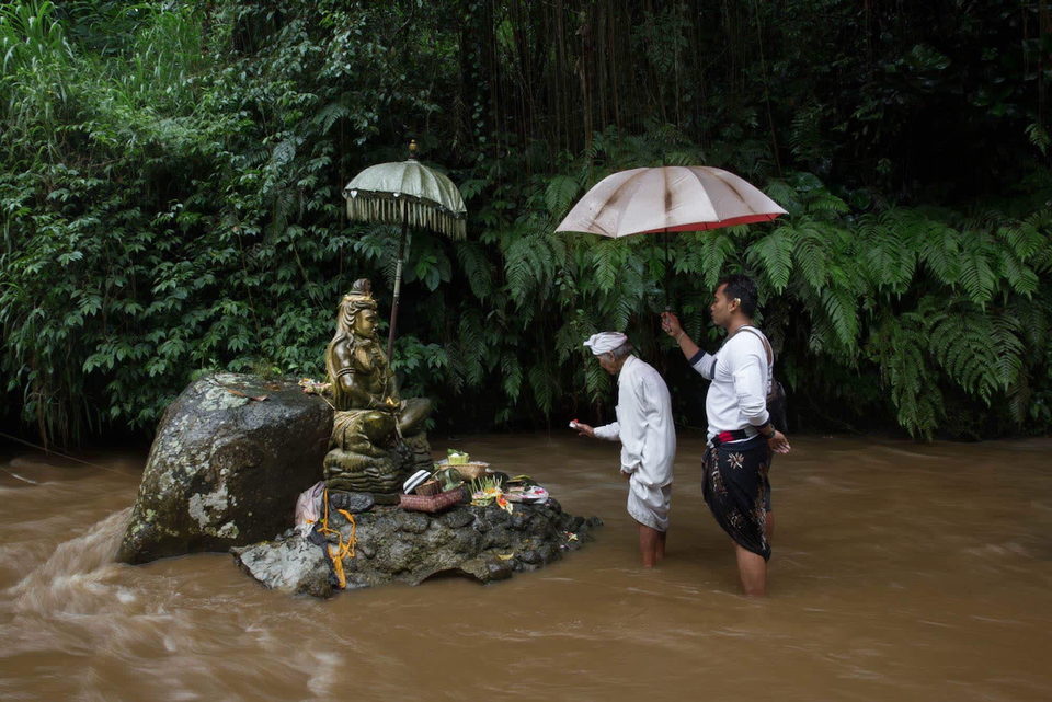 Two men make offerings at a shrine standing in floodwater.