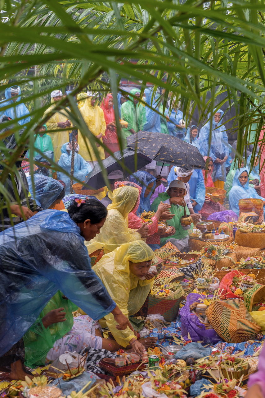 A crowd in coloured rain ponchos gathers around offerings.