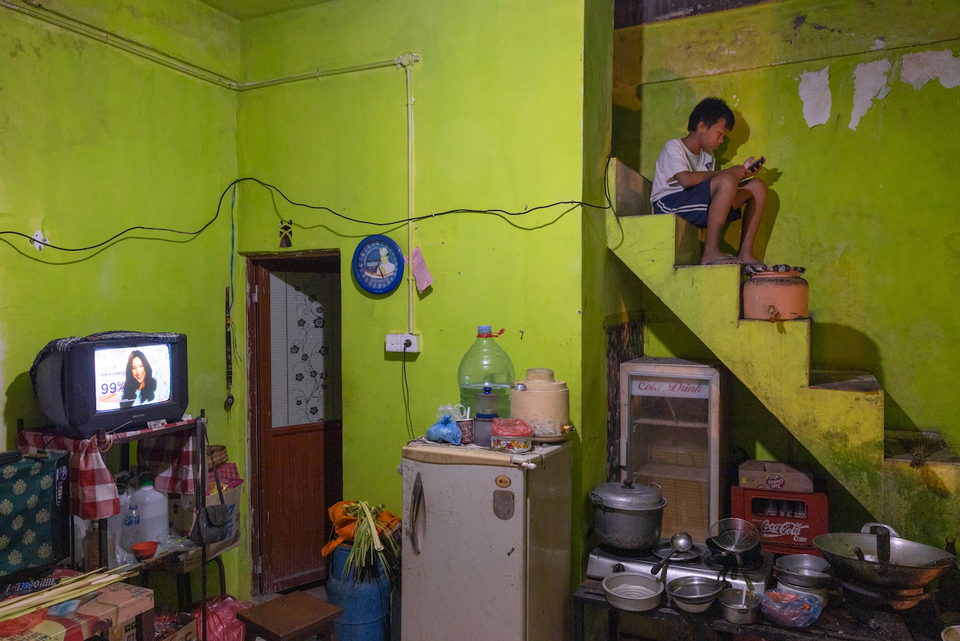 A boy sits on a raised platform above a green-walled kitchen.