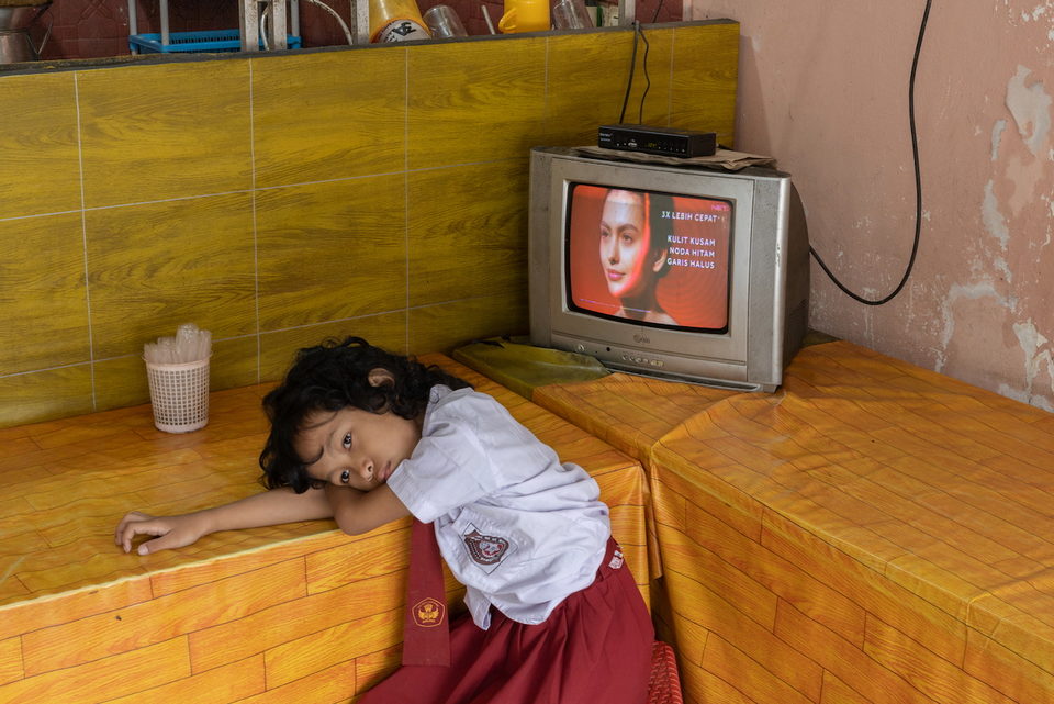 A girl in school uniform rests her head on a bench beside a television.