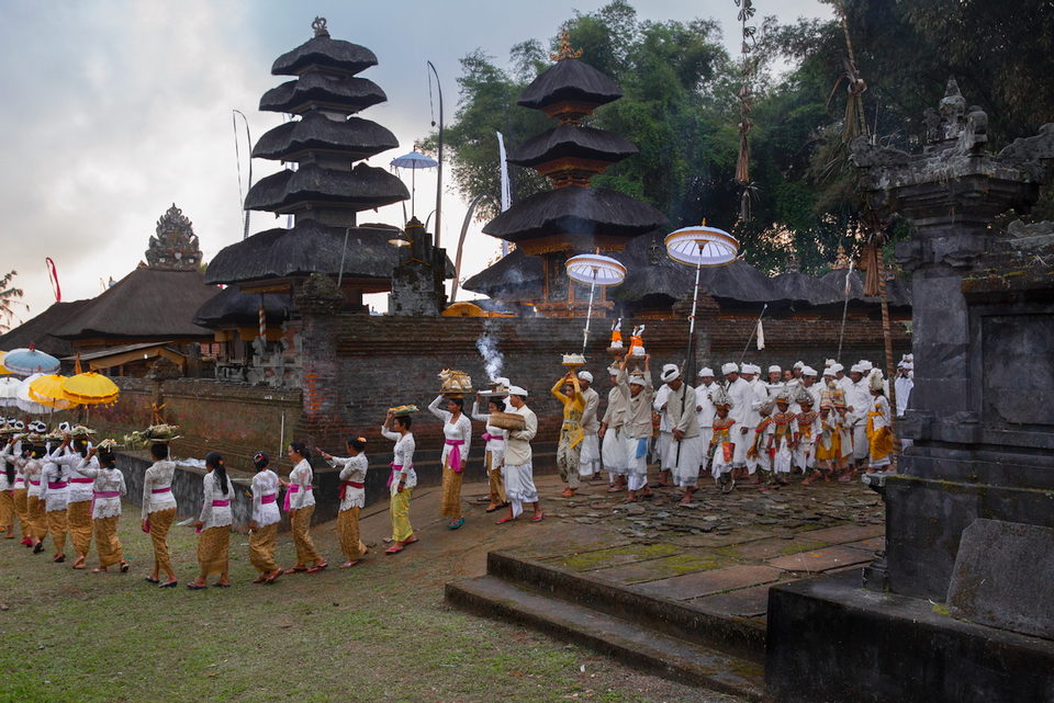 A procession of worshippers passes the tiered meru of a temple.