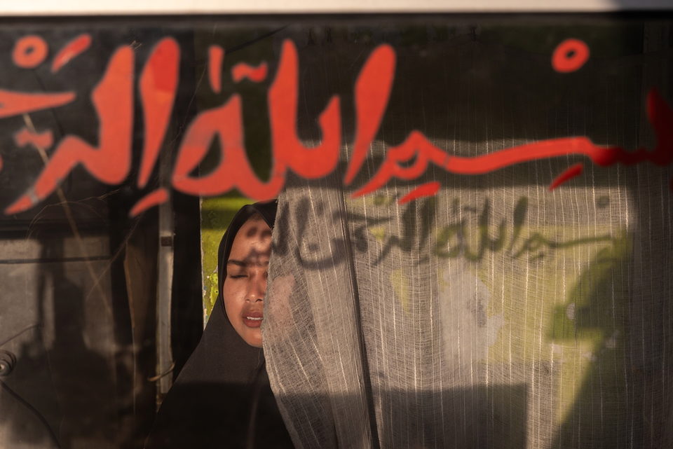 A woman in a headscarf behind glass painted with red Arabic calligraphy.
