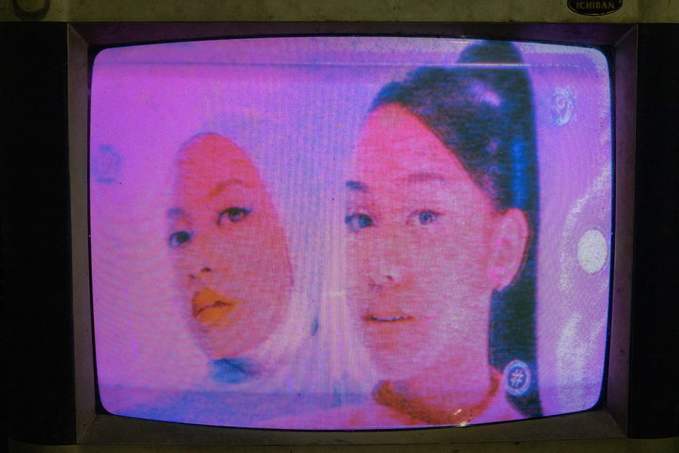 A television close-up of two young women's faces in pink light.