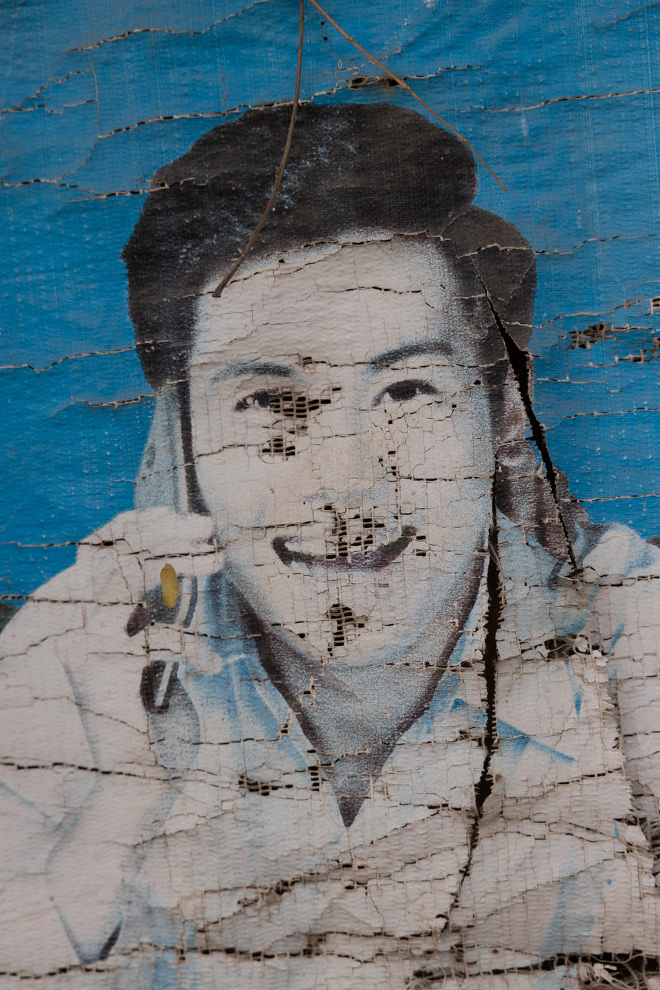 A cracked and weathered mural of a young man's face.