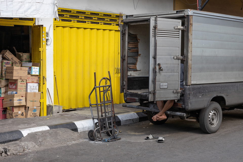A person's legs hang from the back of a truck beside a yellow shutter.