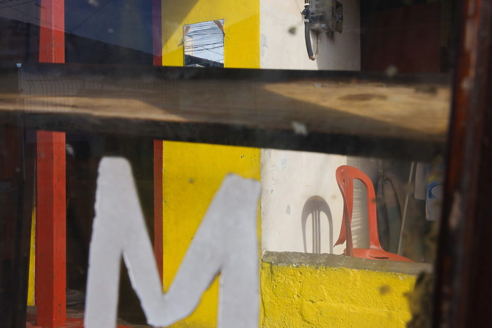 A large white letter M on the cart glass, yellow wall and shadow behind.