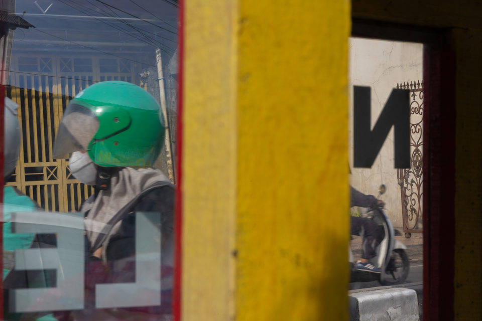 A rider in a green helmet framed by a yellow post and the cart glass.