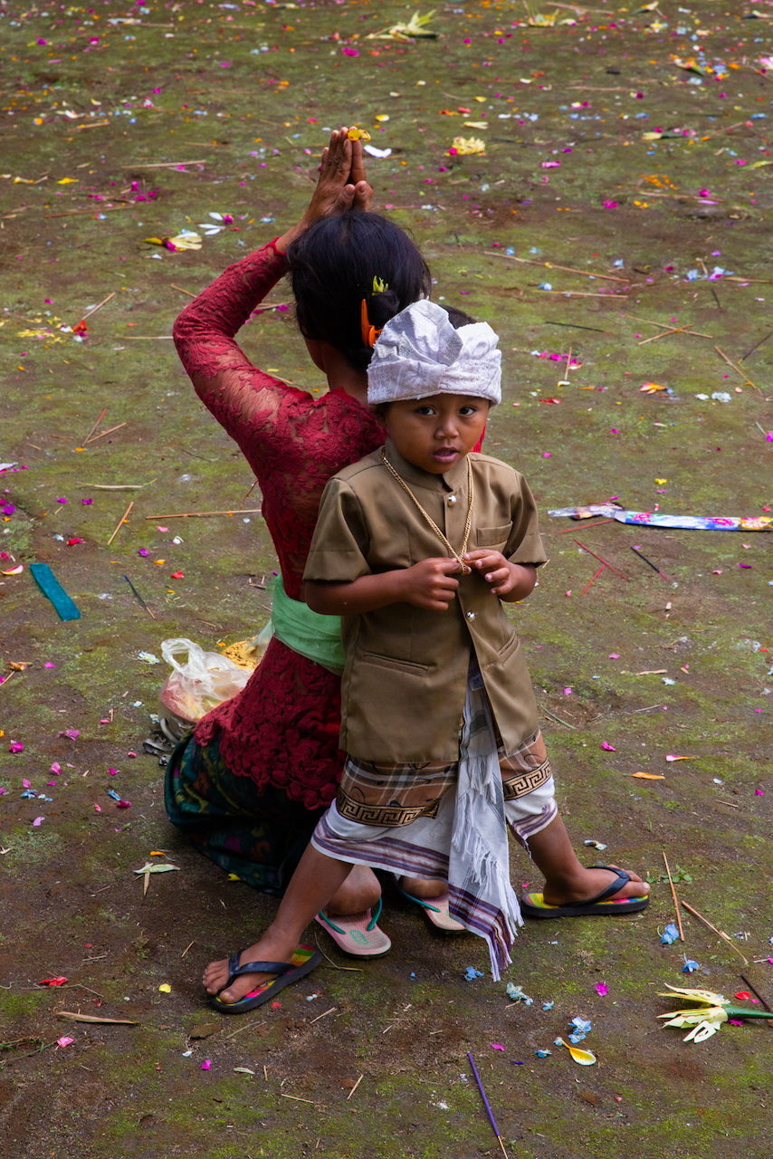 A woman adjusts her hair beside a boy in ceremonial dress, confetti on the ground.