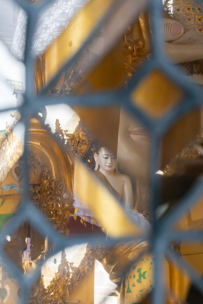 A gilded Buddha statue seen through a lattice of blue and gold mirrored glass.
