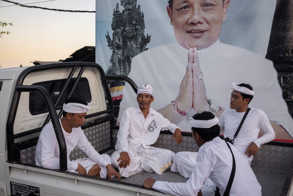 Men in white sit in the back of a truck before a large campaign banner.