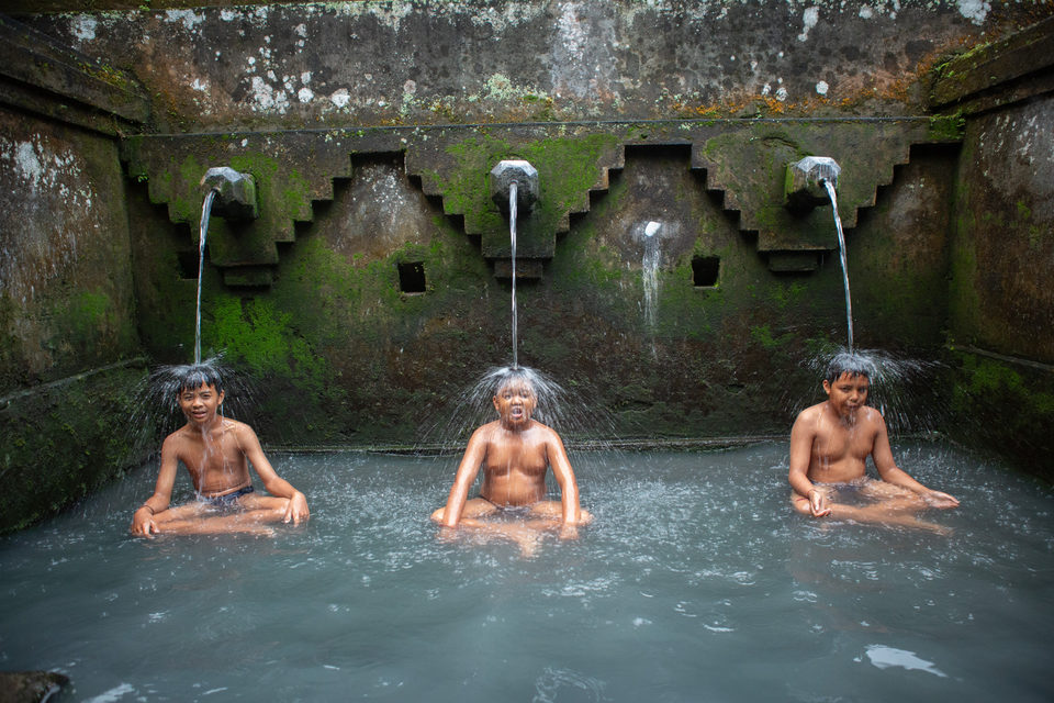 Three men bathe under water spouts at a mossy stone purification pool.