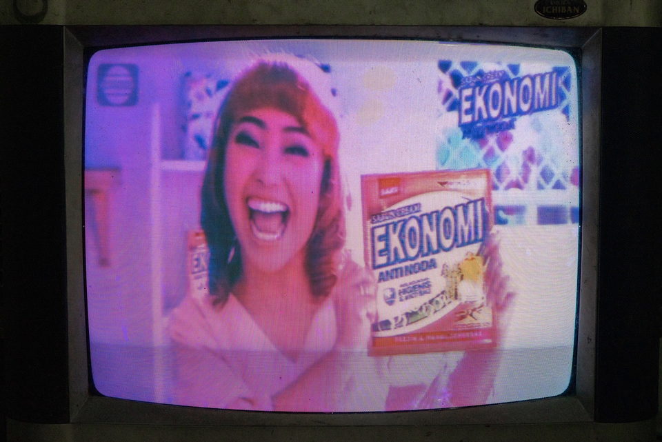 A television advertisement, a woman laughing and holding a detergent box.