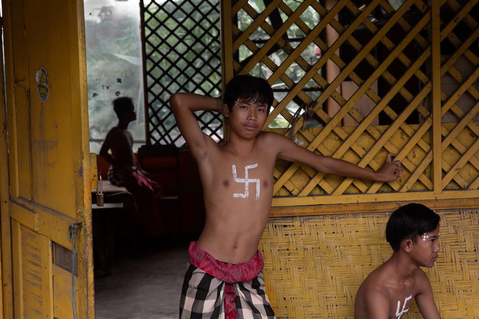 A boy leans against bamboo lattice, a traditional Balinese Hindu symbol painted on his chest.