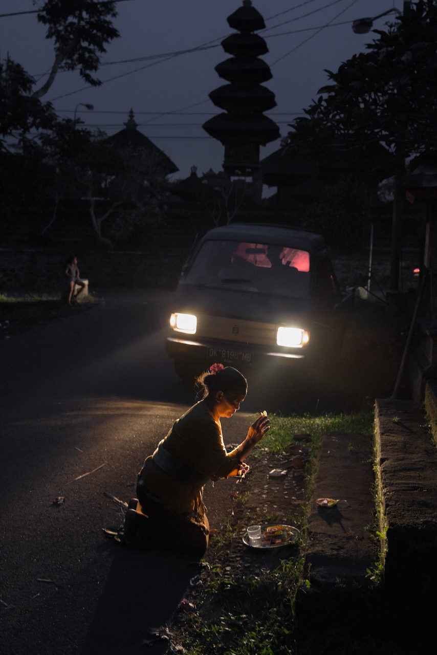 A woman crouches at the roadside lit by the headlights of a truck at night.