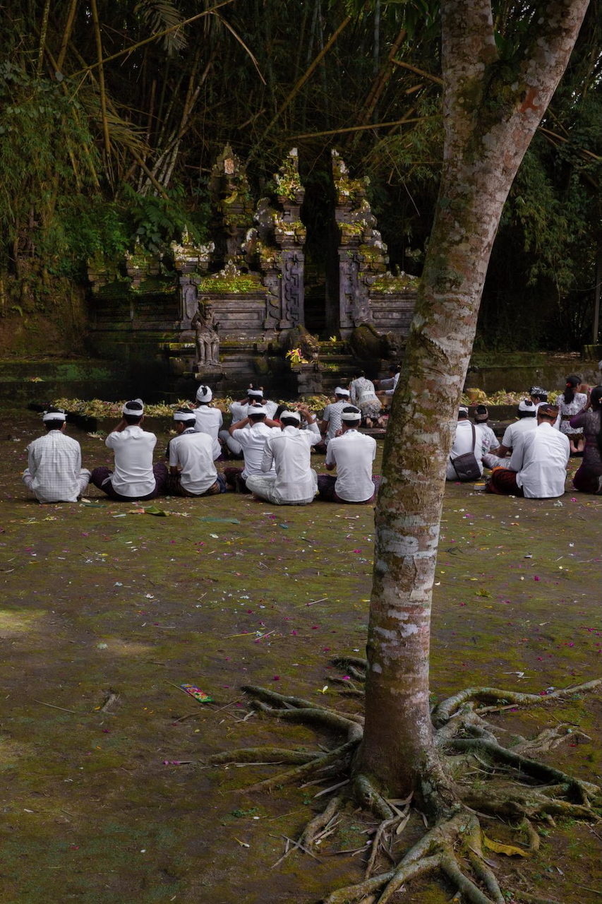 Worshippers in white sit in rows on the ground before a temple shrine.