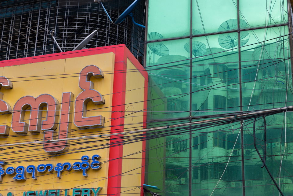 Red and yellow Burmese shop signage against a wall of green mirrored glass.