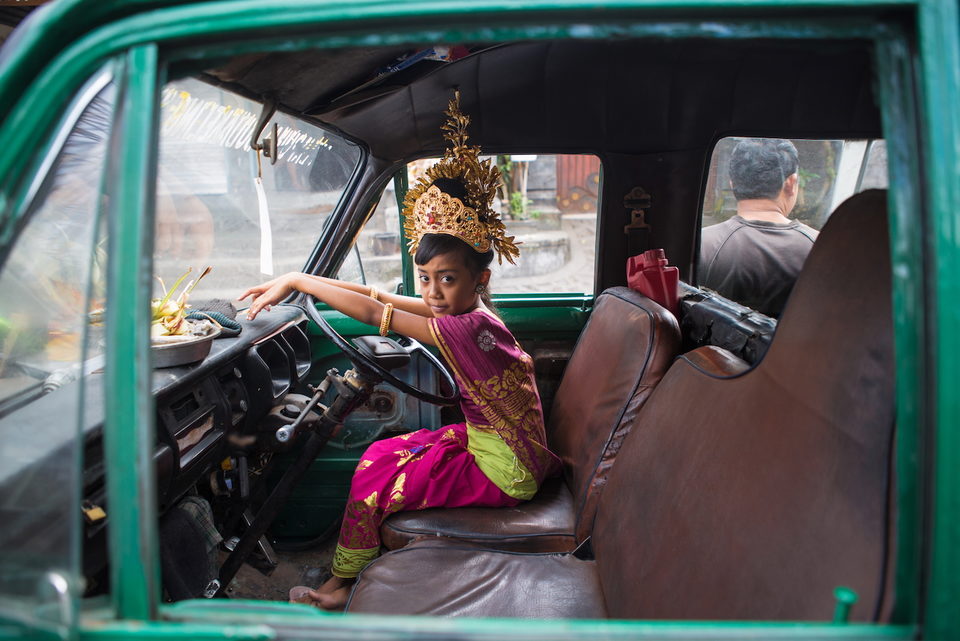 A girl in a gold headdress and pink sash sits in the front of a truck.