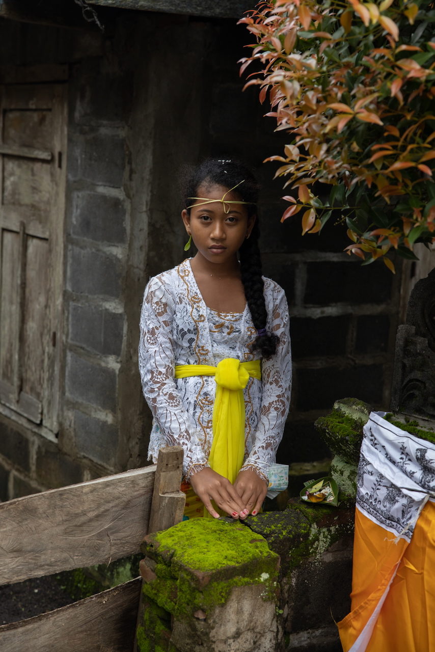 A girl in white lace with a yellow sash stands in a doorway.