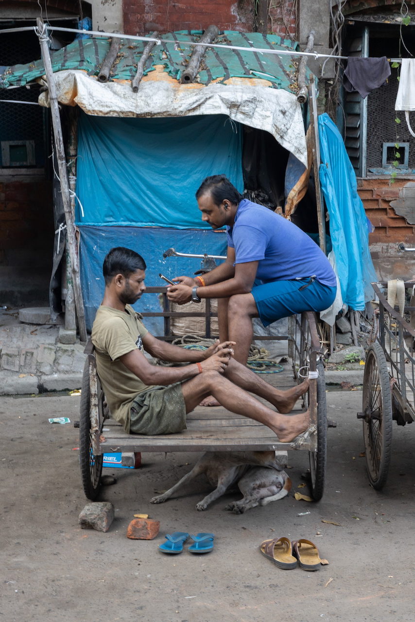 Two men sit talking on a cycle rickshaw.