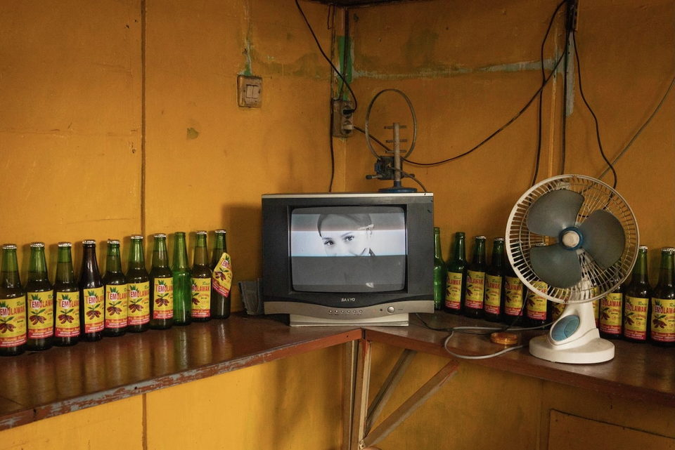 A television on a corner counter lined with bottles.
