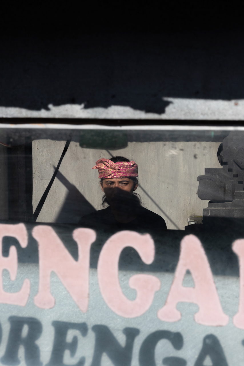 A man in a red headcloth and mask beyond pink lettering.