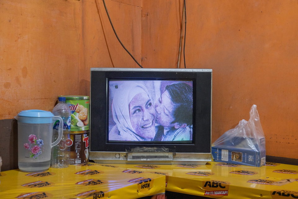 A television showing two women embracing, on a counter of yellow packets.