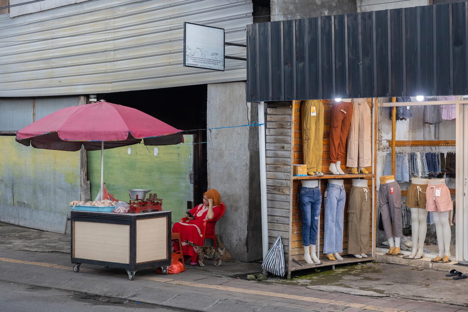 A clothing stall with mannequin legs and a red parasol.